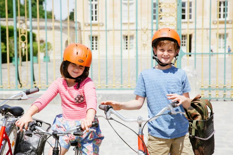 Two children smile next to their bicycles in Versailles, France.