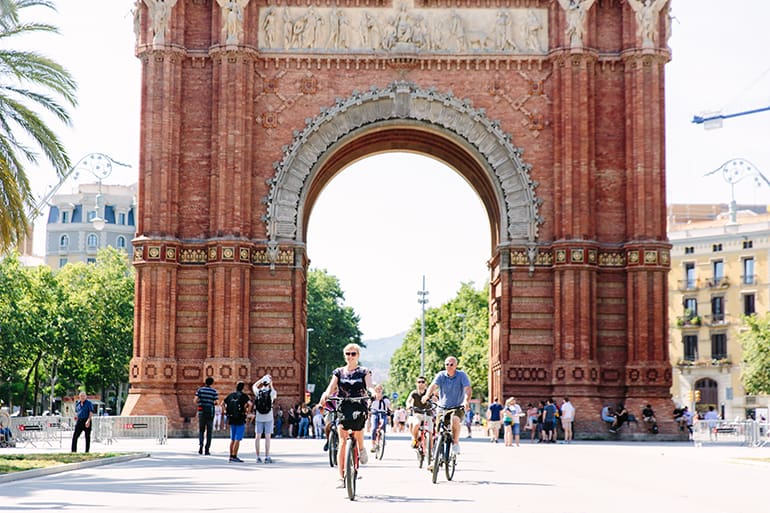 People ride bikes in front of the Arc de Triomf in Barcelona, Spain