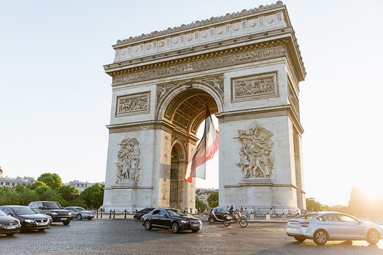 A French flag billows in the arc of the Arc de Triomphe at sunset in Paris, France.