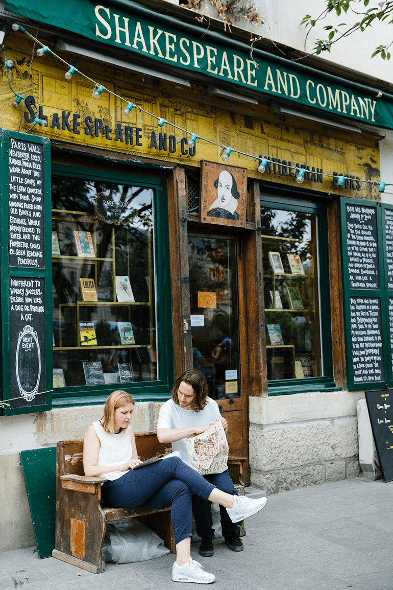 Two people sit on a bench and read a book outside Shakespeare and Company bookstore in Paris, France.