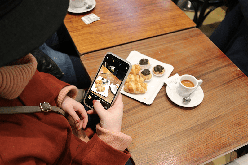 Woman takes a photo on her iPhone of her espresso and Italian pastries.