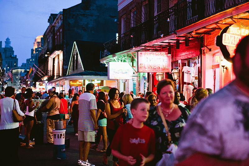 Crowds of people walk down Bourbon Street, New Orleans at night.