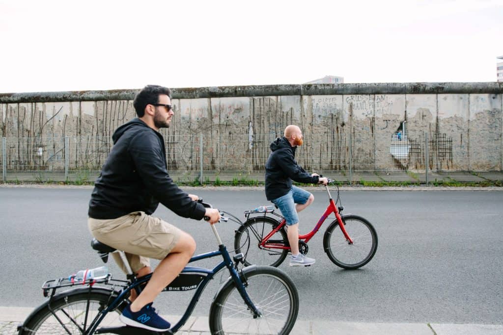 Two men on bicycles cruise alongside the remains of the Berlin Wall in Germany.