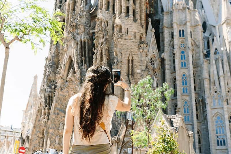 Brunette woman takes a photo of La Sagrada Familia on her iPhone in Barcelona.