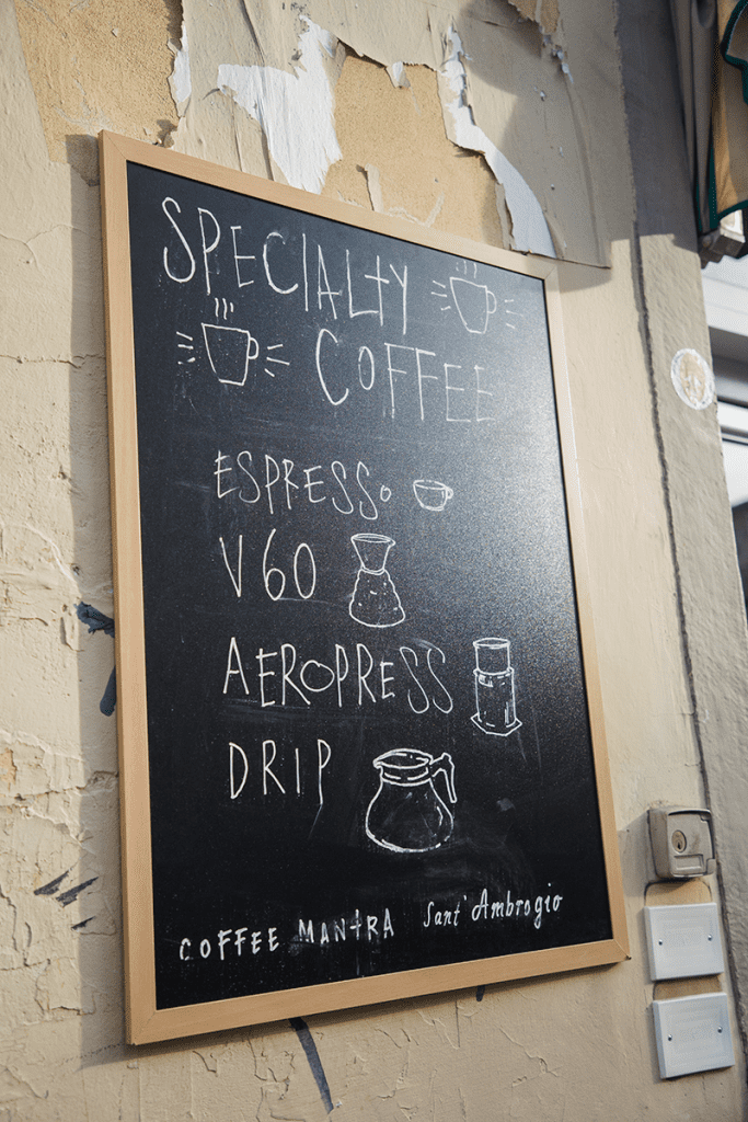 A chalkboard sign advertising types of coffee and espresso offered outside a shop in Italy