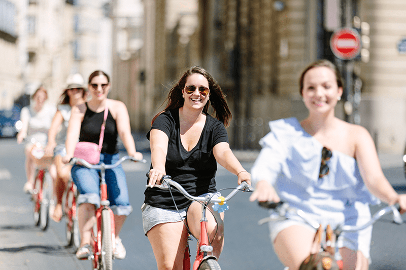 A row of people smile as they ride bicycles through the streets in Paris, France