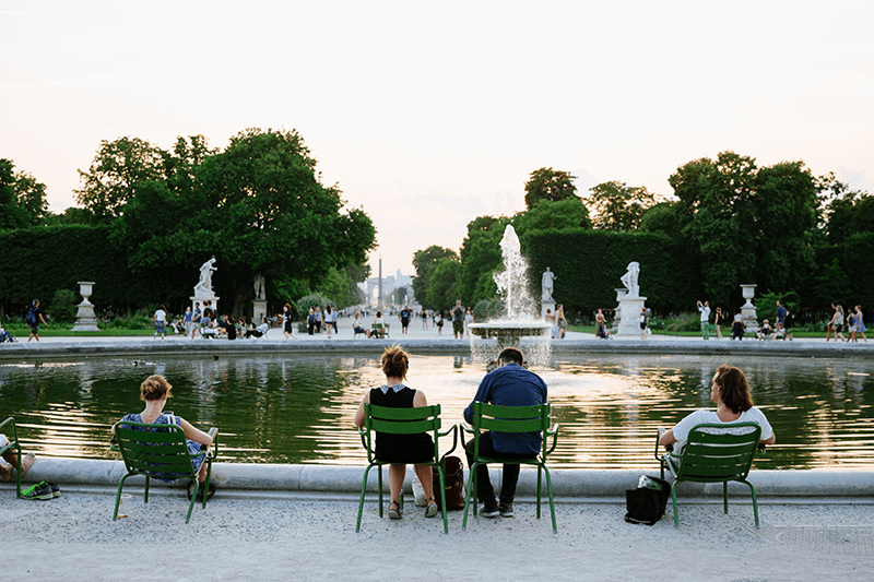 People relax in the famous green lounge chairs in front of a pond in the Tuileries Gardens in Paris, France at sunset.