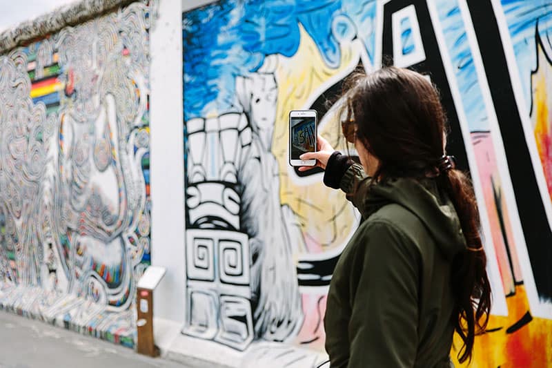 Woman takes a photo of the East Side Gallery street art in Berlin, Germany