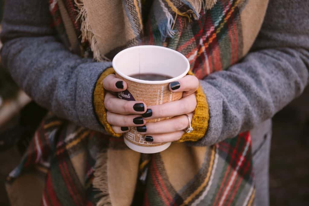 woman holding cup of hot wine bundled up in coat and scarf at the paris christmas market