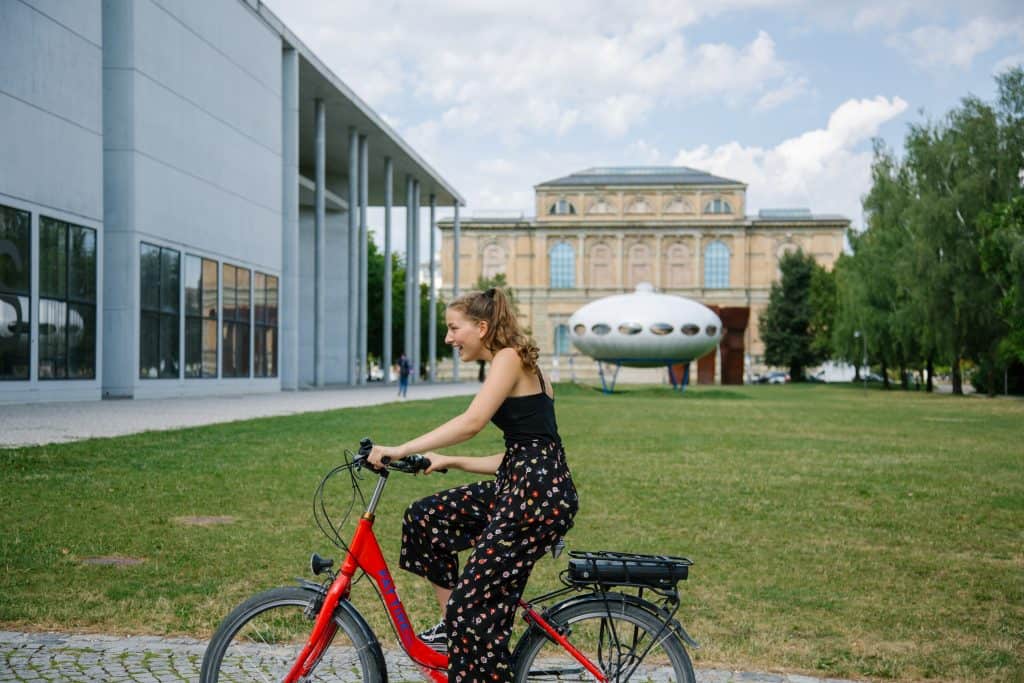 Girl riding a bicycle in front of Pinakothek der Moderne Futuro House in Munich, Germany