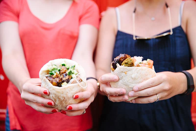 Two women hold up falafel sandwiches from L'as du Fallafel in the Marais of Paris, France