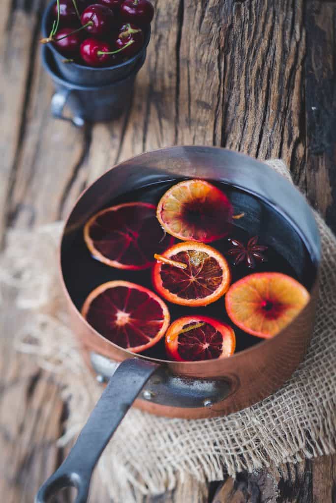 mulled wine being prepared with orange slices, star anise, and cinnamon in a copper pot as a cozy winter drink