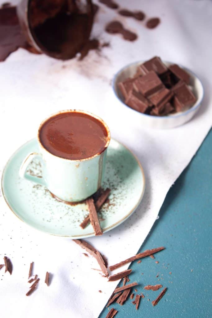 thick homemade hot chocolate as a cozy winter drink with bowl of chocolate pieces