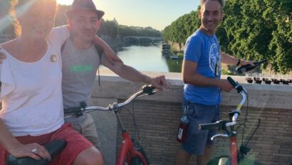 A guide pours wine while a couple smiles for a photo on their bikes in Rome, Italy