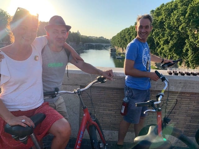 A guide pours wine while a couple smiles for a photo on their bikes in Rome, Italy