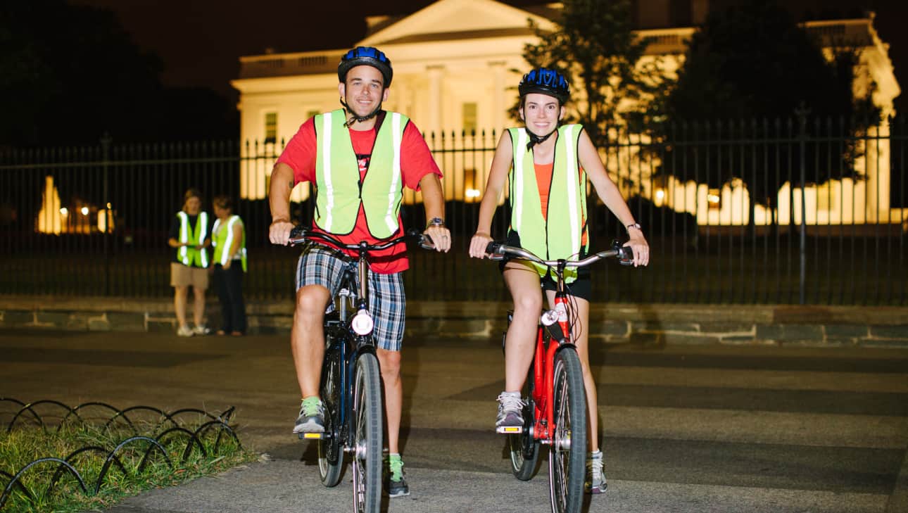 two people on bikes with reflective vests in front of the white house