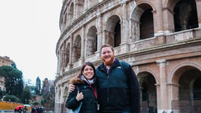 A couple poses for a photo in front of the Colosseum in Rome, Italy