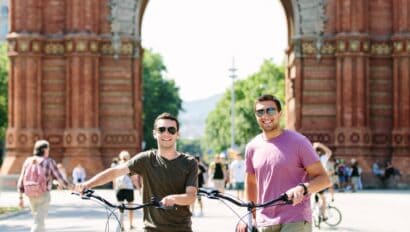 Two men pose with their bikes in front of the Arc de Triomf in Barcelona, Spain