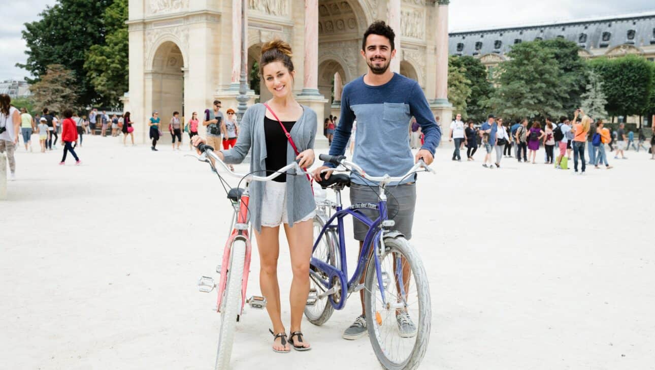 A couple poses with their bikes in front of the Arc de Trimophe du Carrousel in Paris, France