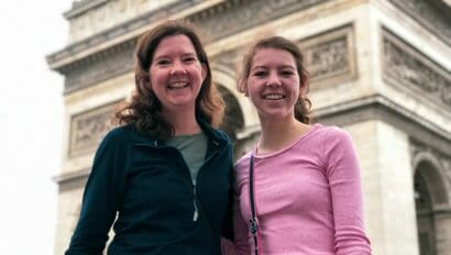 A mother and daughter smile for a photo in front of the Arc de Triomphe in Paris, France