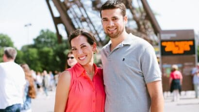 A couple poses for a photo at the base of the Eiffel Tower in Paris, France