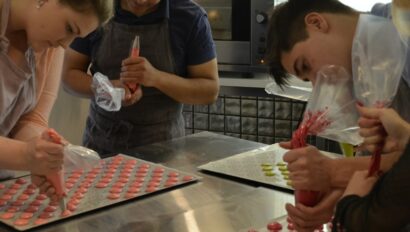 Three people pipe colorful macarons onto baking sheets in Paris, France