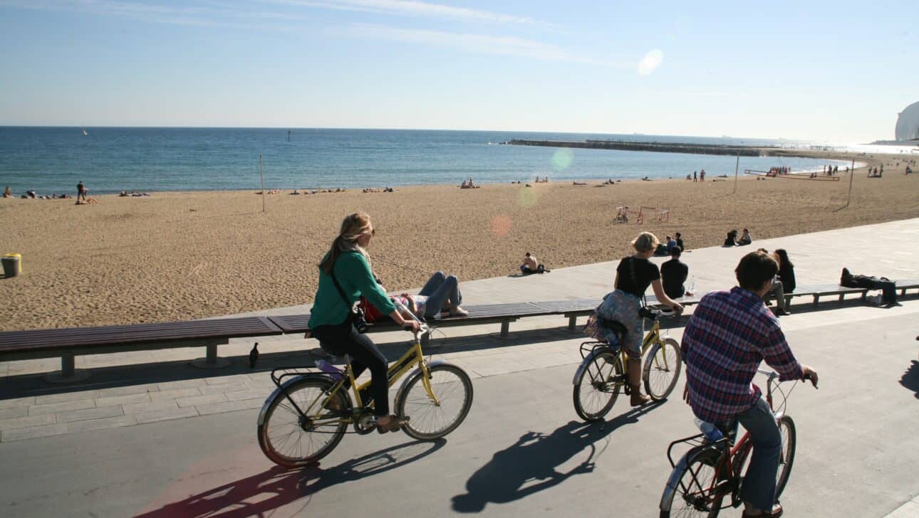 Three people ride bikes along the beach in Barcelona, Spain
