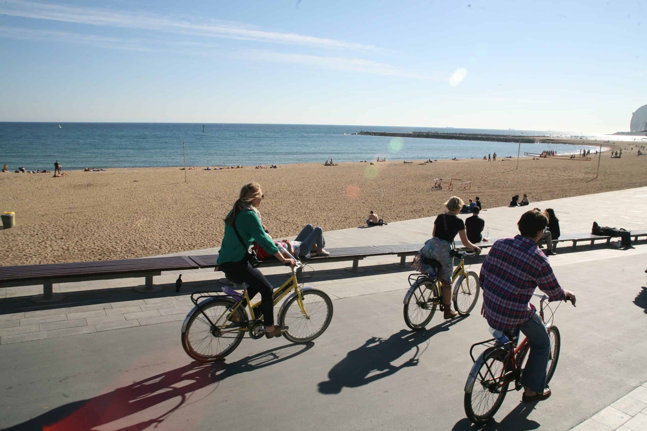 Three people ride bikes along the beach in Barcelona, Spain