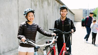 Two people pose with their bikes in front of the Berlin Wall in Berlin, Germany