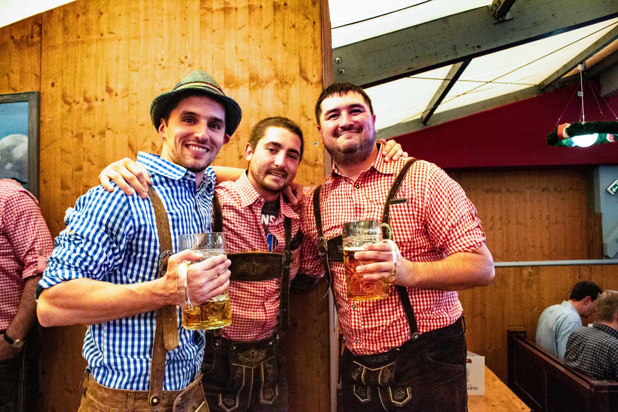 Three men at Oktoberfest drinking beers and dressed in liederhosen