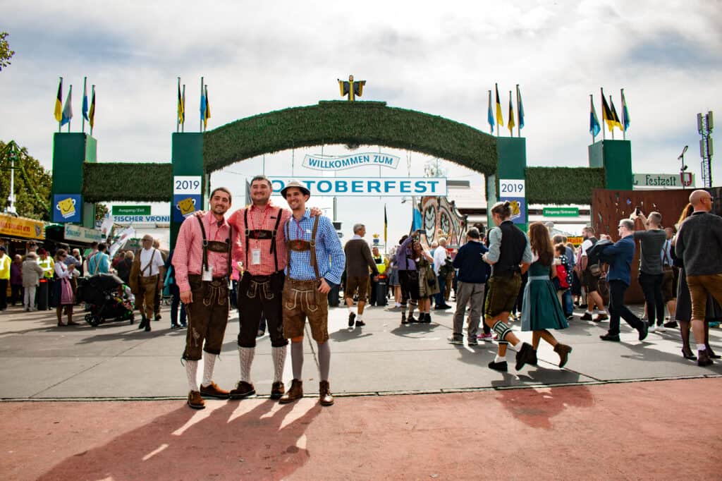 Three men dressed in traditional Bavarian clothing stand outside of Oktoberfest in Munich