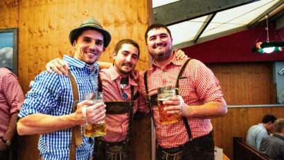 Three men hold their litres of beer dressed in traditional lederhosen at Oktoberfest in Munich, Germany