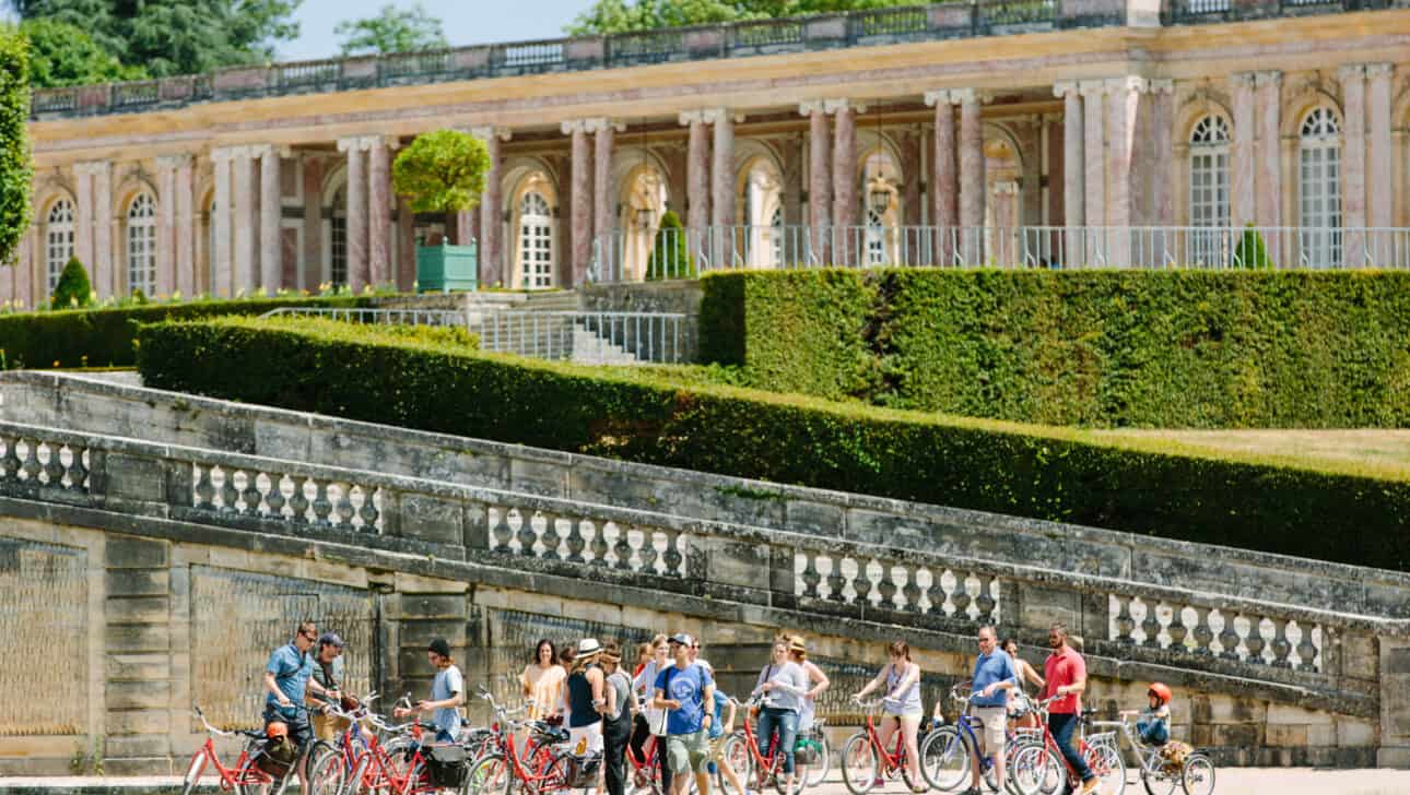 A group of cyclists stop near the Grand Trianon to learn about it from their tour guide during the Versailles Bike Tour.