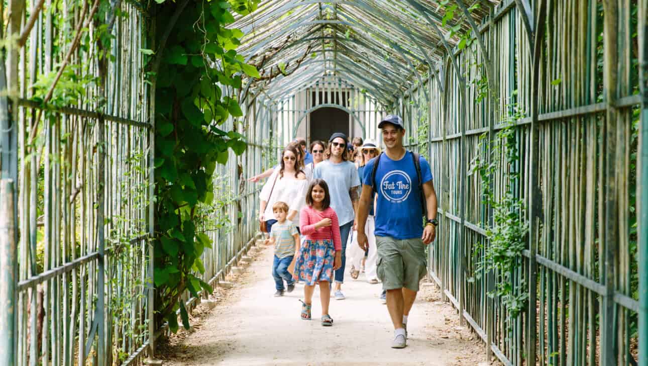 A tour guide in a blue t-shirt walks through the gardens of Versailles with his group.