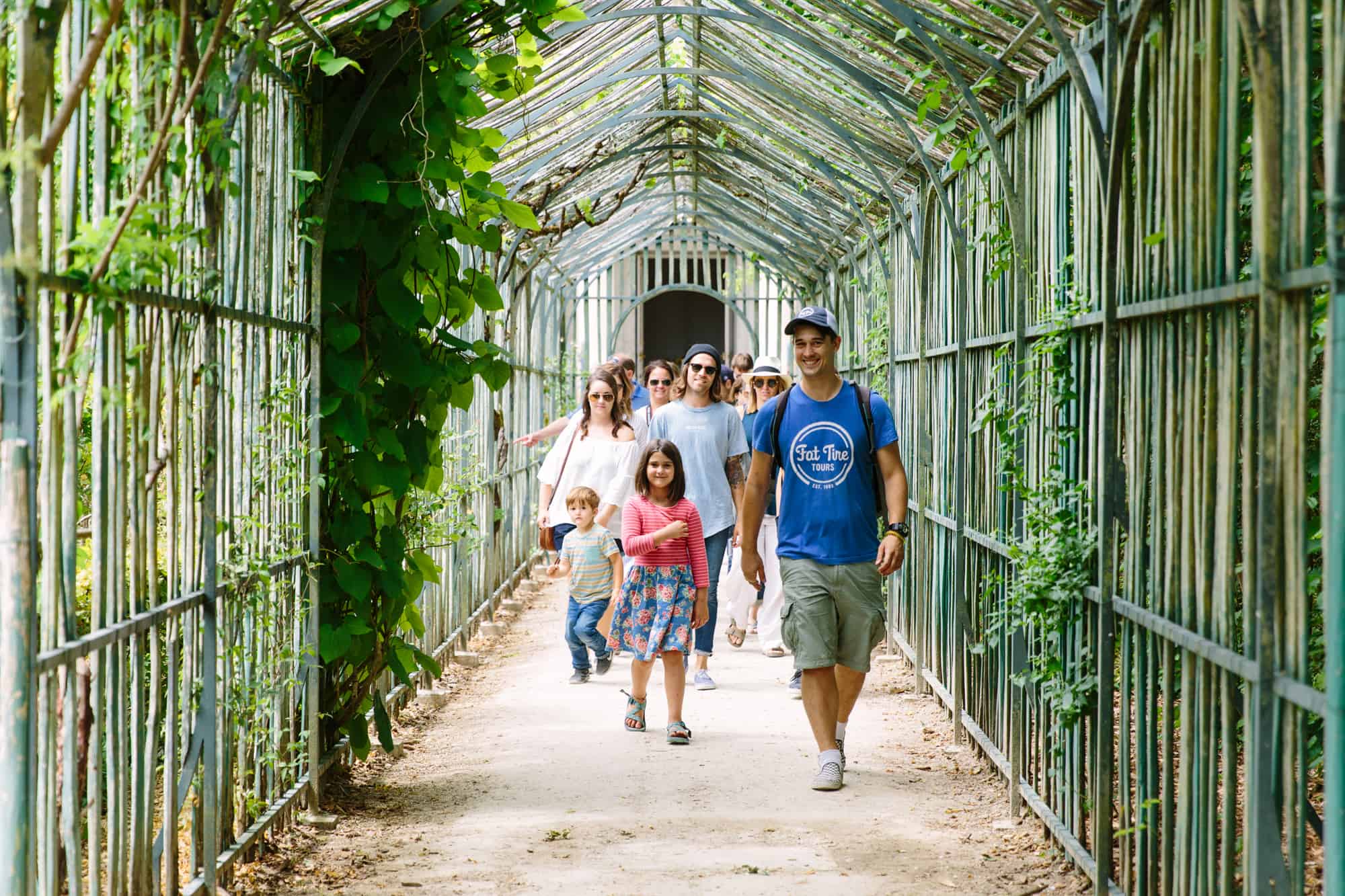 A tour guide in a blue t-shirt walks through the gardens of Versailles with his group.