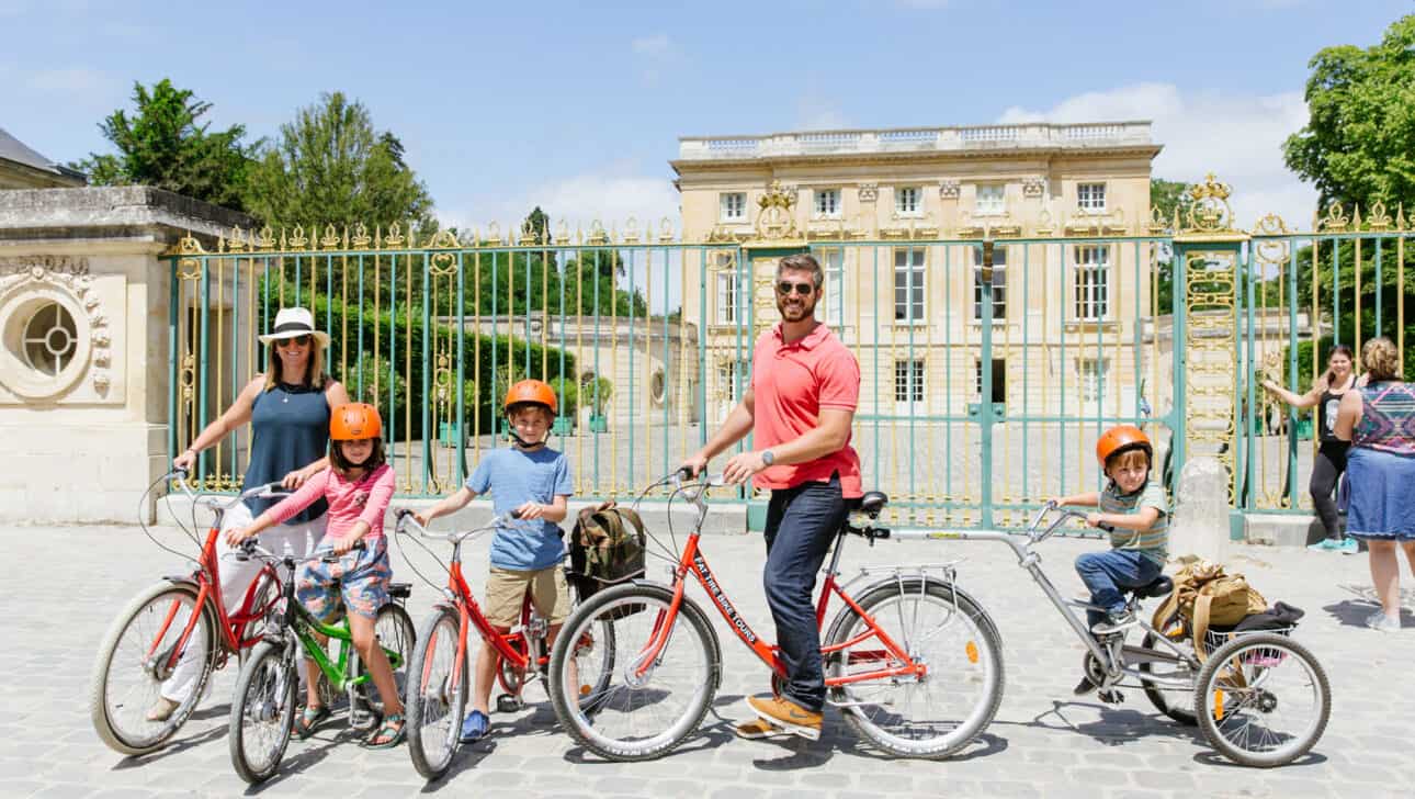 A family of five poses with their bikes in front of the Petit Trianon during the Versailles Bike Tour.