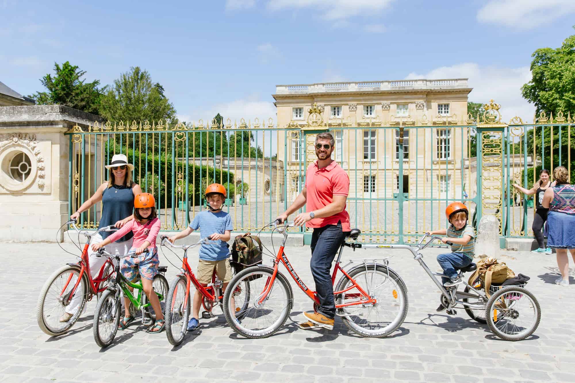 A family of five poses with their bikes in front of the Petit Trianon during the Versailles Bike Tour.