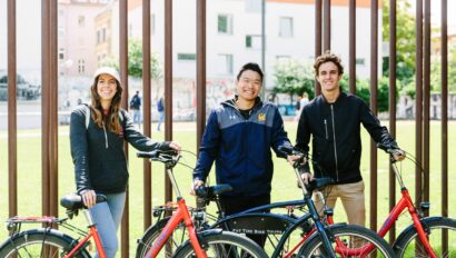 A group of three poses with their bikes in front of the Berlin Wall in Berlin, Germany