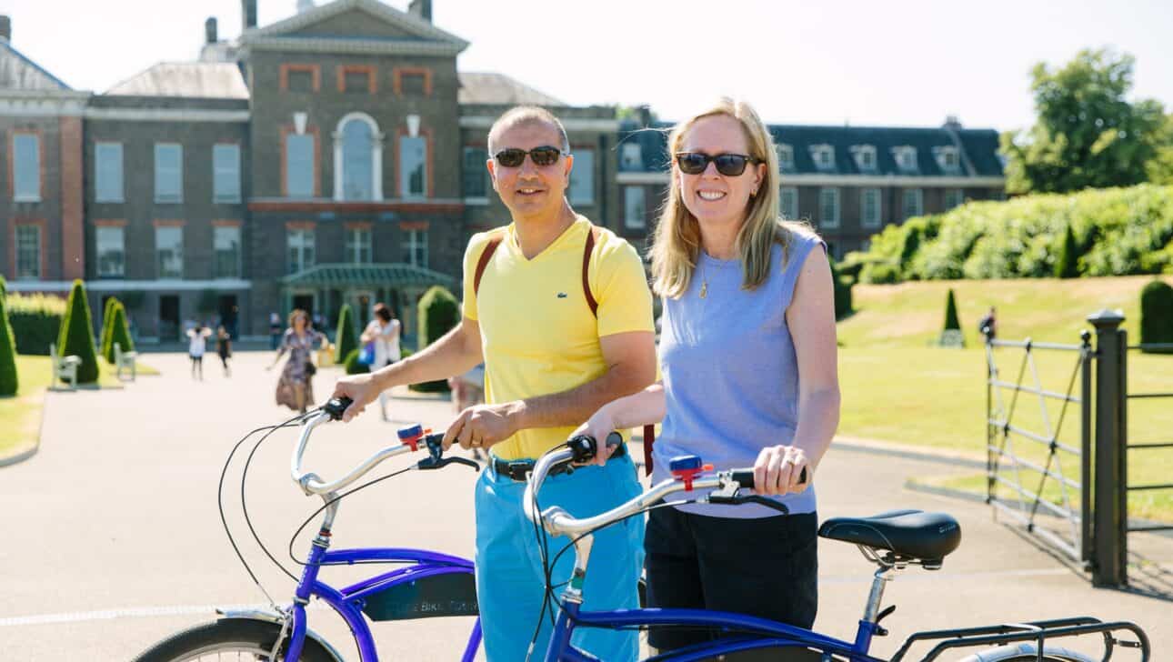 A couple poses with bikes in front of Kensington Palace in London, England