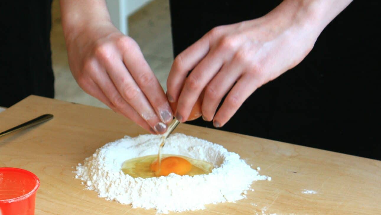 A guest makes authentic Italian pasta by cracking an egg into flour in Rome, Italy