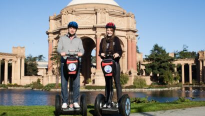 Two people smile for a photo on Segways in front of the Palace of Fine Arts in San Francisco, California
