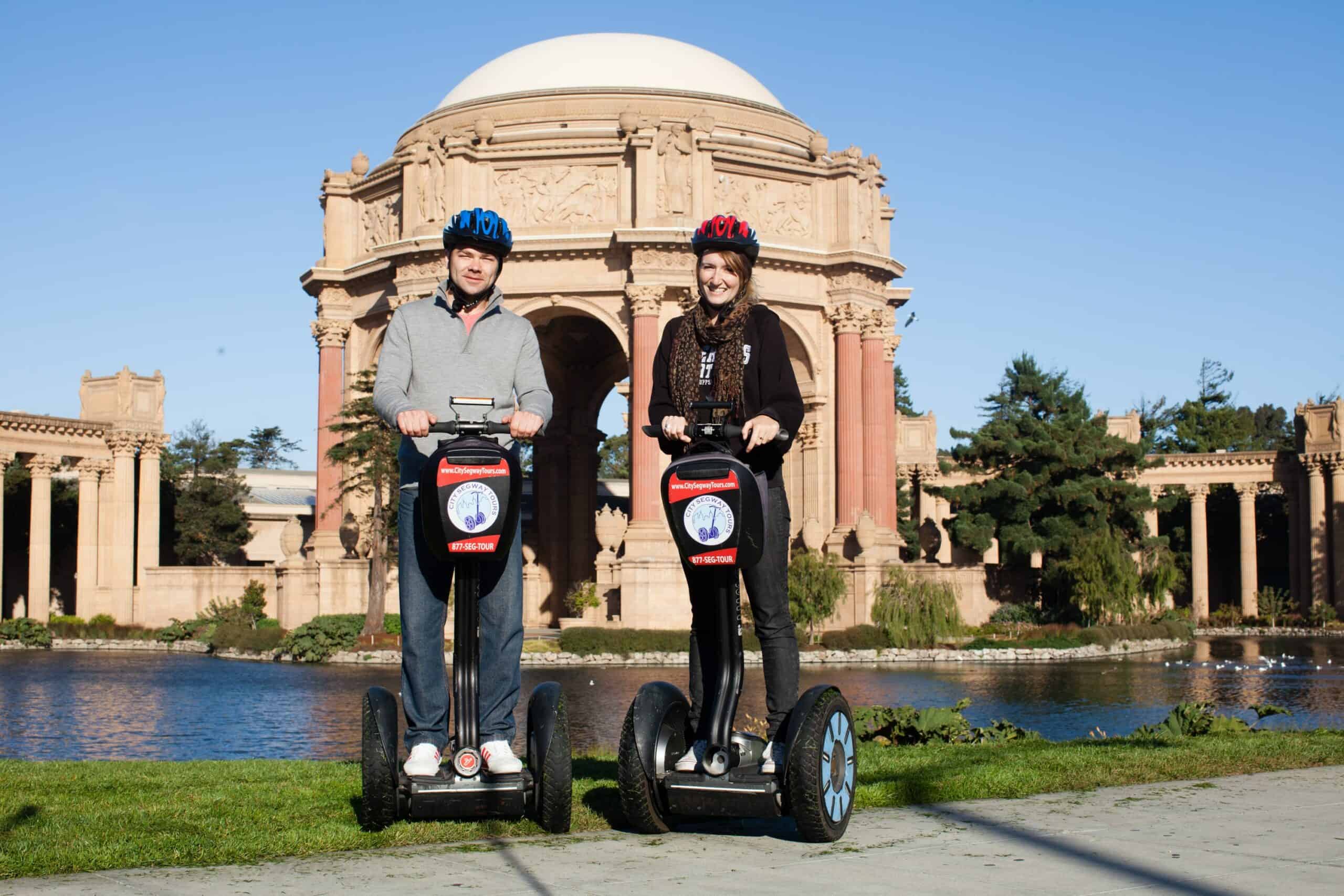 Two people smile for a photo on Segways in front of the Palace of Fine Arts in San Francisco, California