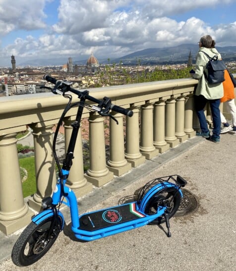 Two people look out over Florence, Italy while their e-scooter is parked off to the side
