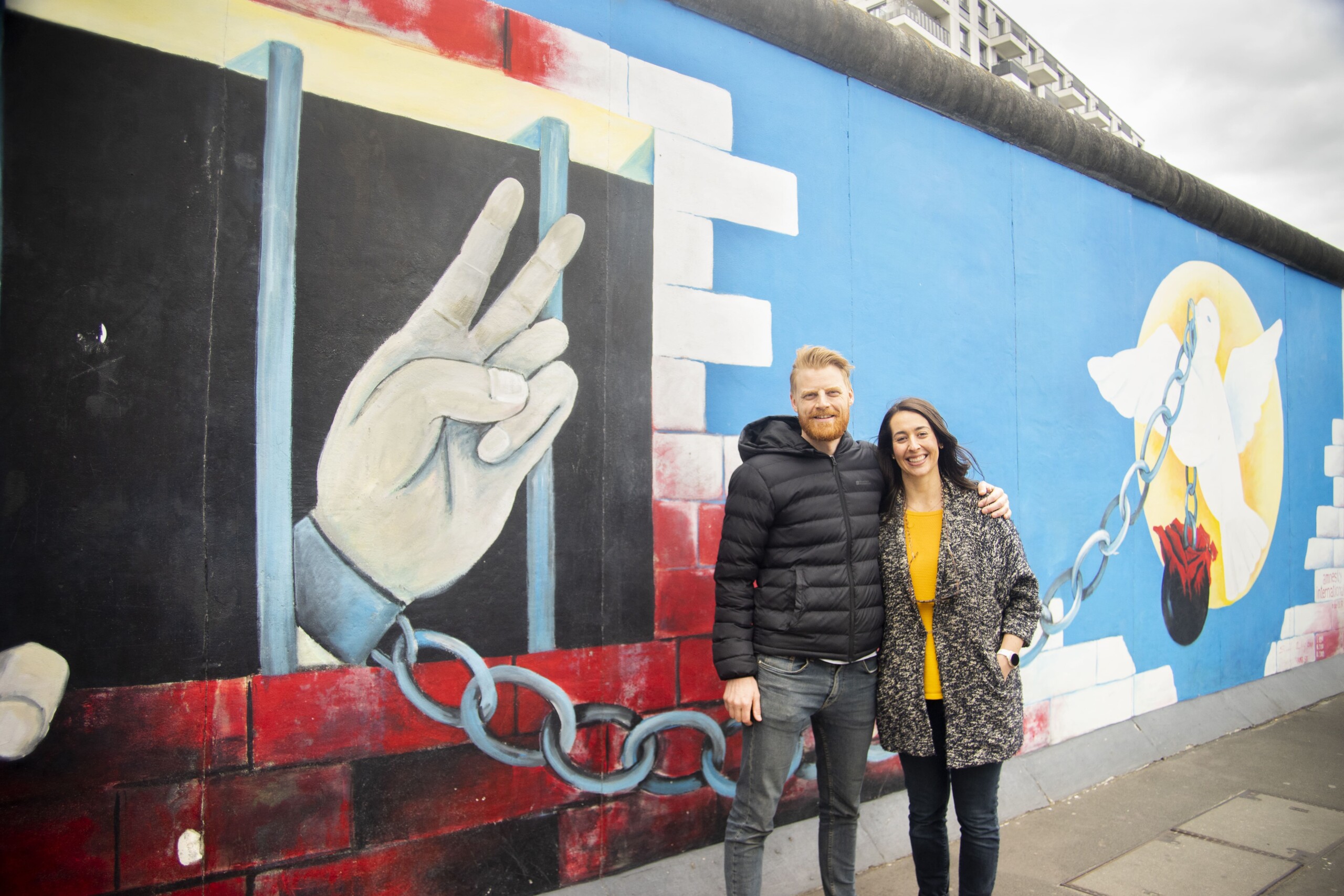 A couple poses in front of the East Side Gallery in Berlin, Germany