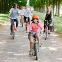 A little girl rides a bike along a tree-lined path