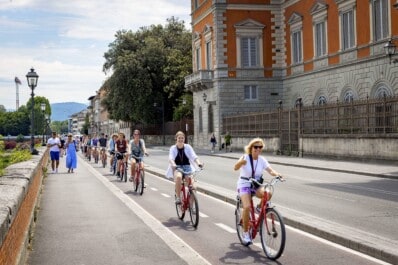 A group of cyclists rides alongside the river Arno in Florence, Italy