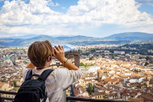 A young boy looks through a viewfinder out over the city of Florence