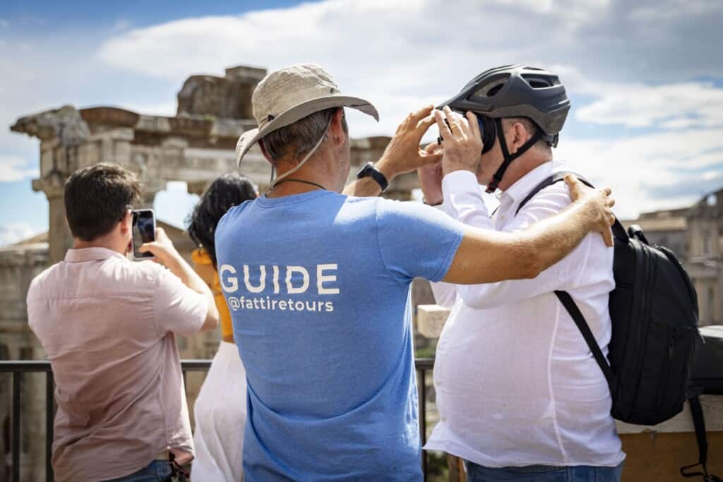 A Fat Tire Tours guide wearing a tan hat helps a customer on tour as he explores Rome
