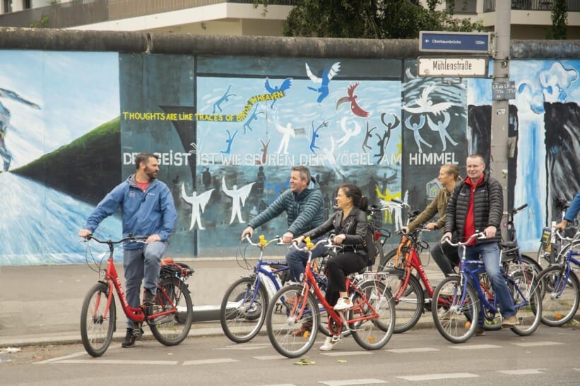 A group of cyclists pauses in front of the East Side Gallery in Berlin, Germany