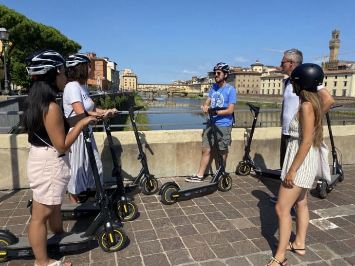 A group gathers on a bridge in Florence, Italy along with their e-scooters